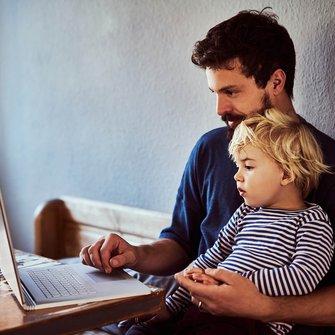 Ein Vater schaut mit seinem kleinen Sohn in einen Laptop.