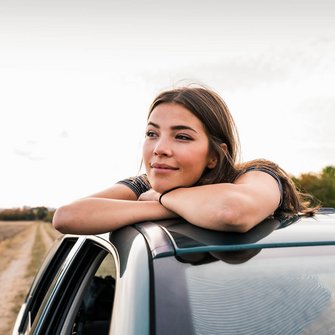 Eine junge Frau schaut aus dem Schiebedach ihres Autos.