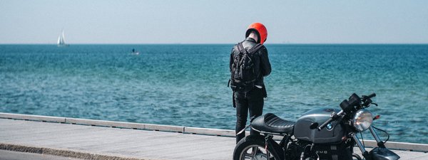 Ein junger Mann steht mit seinem Motorrad am Meer.