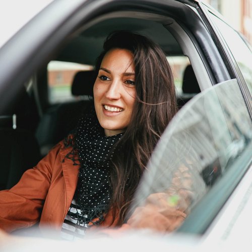 Eine junge Frau sitzt bei geöffnetem Fenster im Auto.