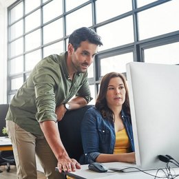 Zwei Arbeitskollegen schauen auf einen Computerbildschirm.