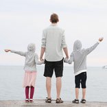 Ein Vater steht mit seinen beiden Kindern am Meer.