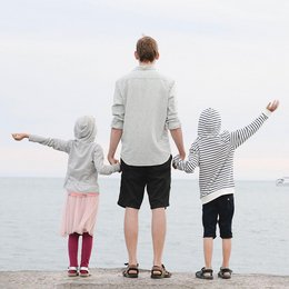 Ein Vater steht mit seinen beiden Kindern am Meer.